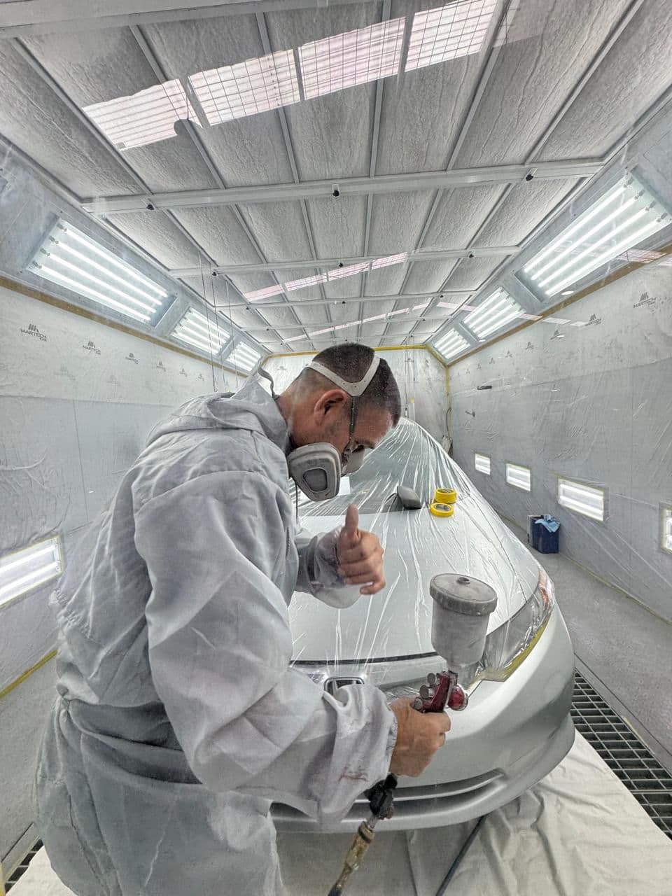 Técnico aplicando pintura con pistola en cabina de pintura profesional